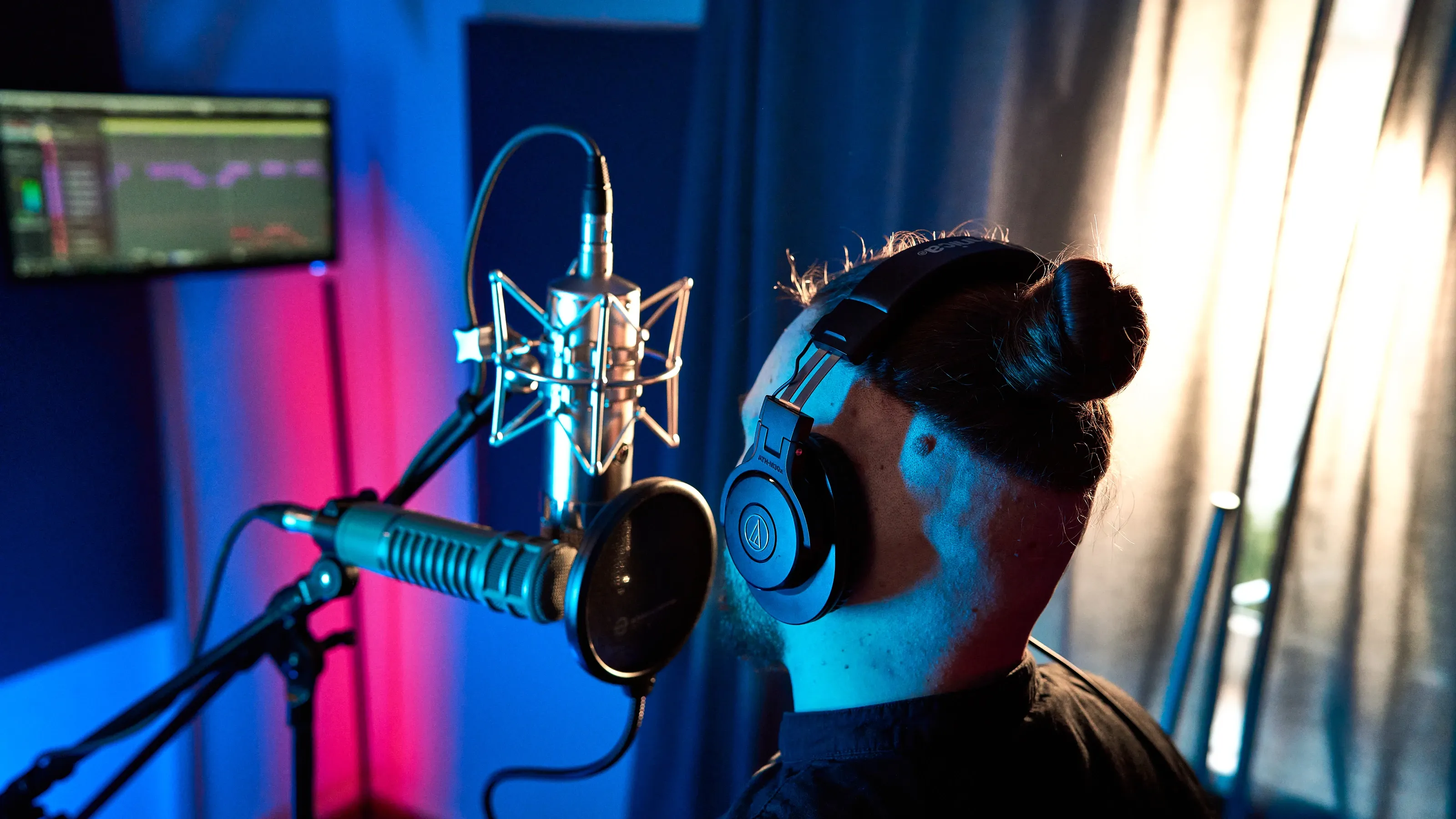 Wokalista w słuchawkach przed mikrofonem i pop filtrem w niebieskim świetle Tetra Wave Studio.
