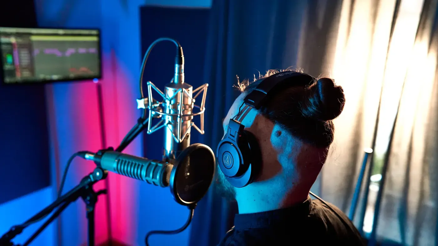 Wokalista w słuchawkach przed mikrofonem i pop filtrem w niebieskim świetle Tetra Wave Studio.